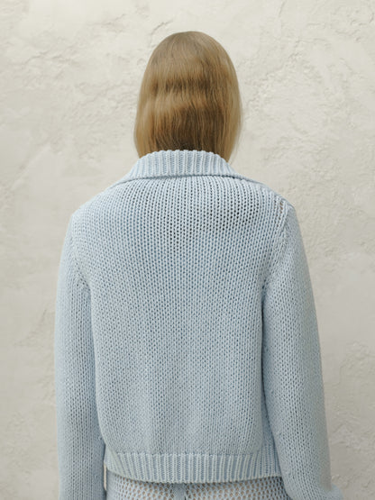 Back view of a model wearing a light blue chunky knit bomber jacket with a ribbed collar and hem.
