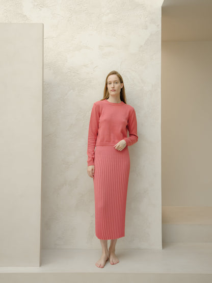 Front view of a model wearing a rose pink Fine Cotton Plissé Long Skirt with a matching knit sweater in a minimalist studio.