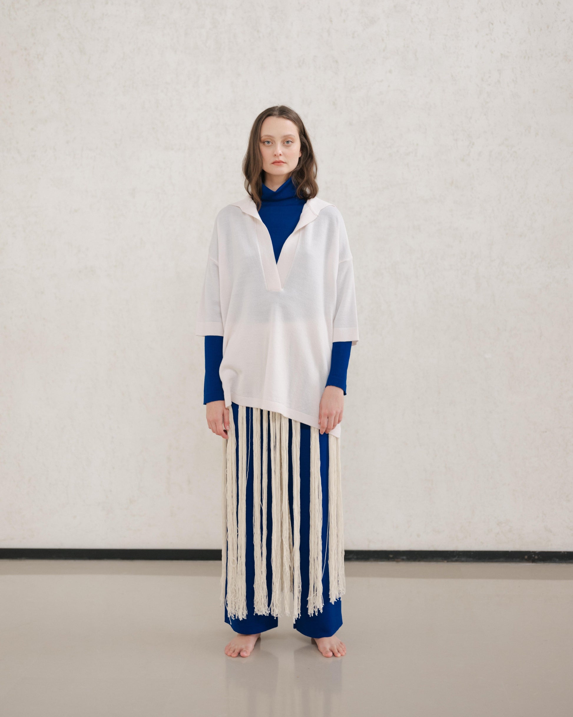 Model wears a pale cream Extra Fine Merino Wool Maxi Polo with a royal blue underlayer and a long fringe skirt.