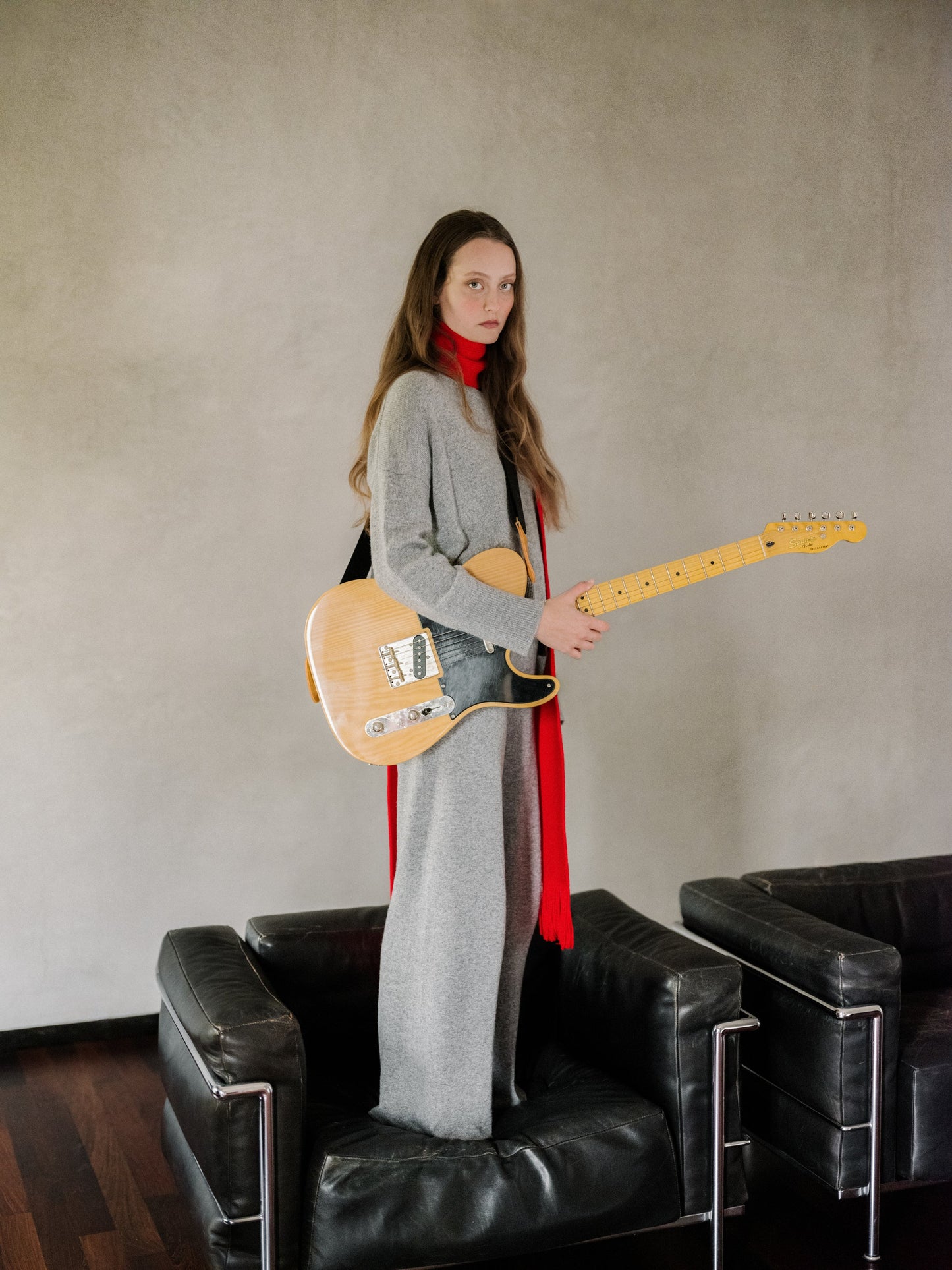 Model wearing a gray cashmere mix crewneck sweater as part of a layered outfit with a red scarf while holding an electric guitar