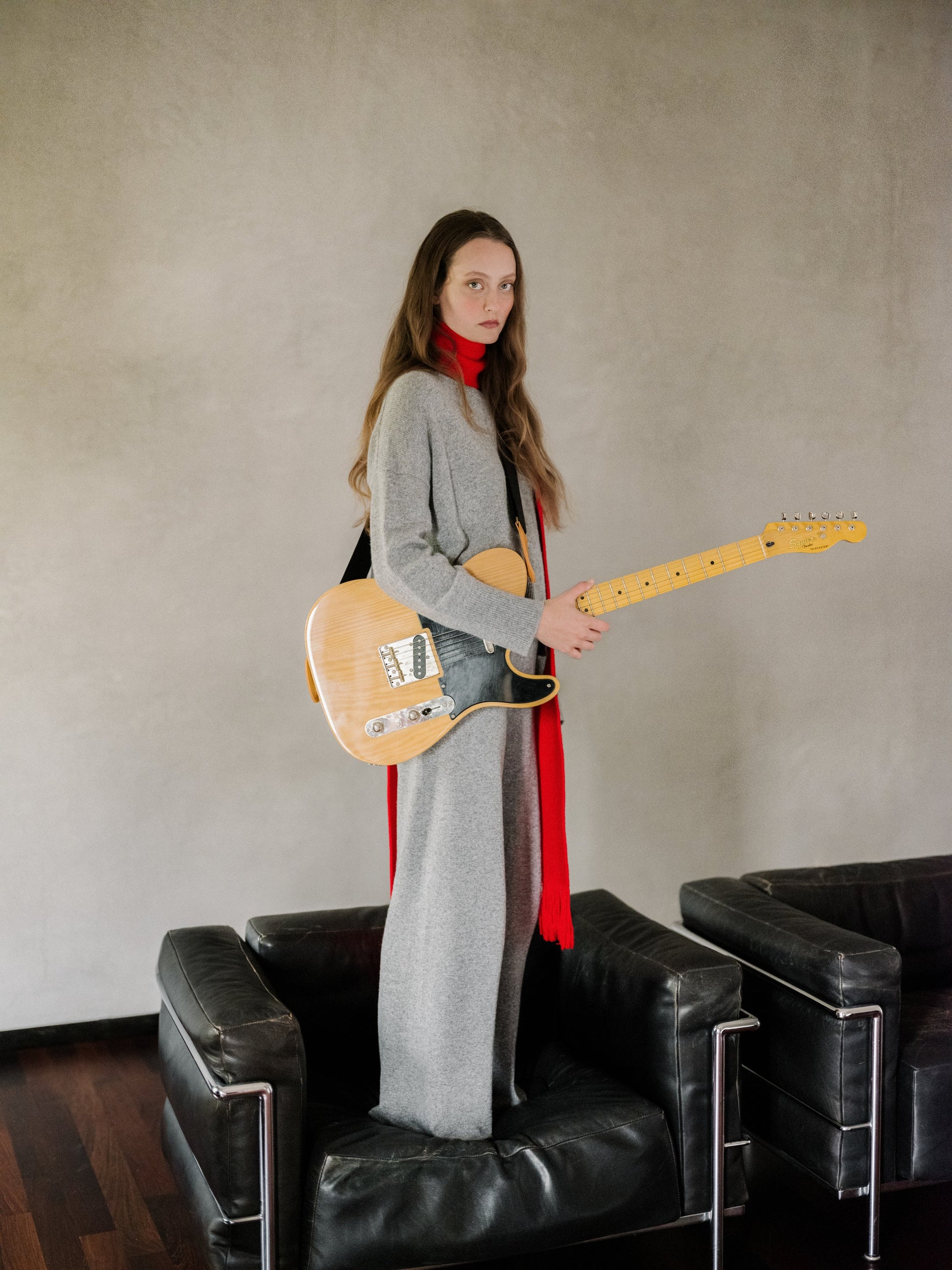 Model wearing a gray cashmere mix crewneck sweater as part of a layered outfit with a red scarf while holding an electric guitar