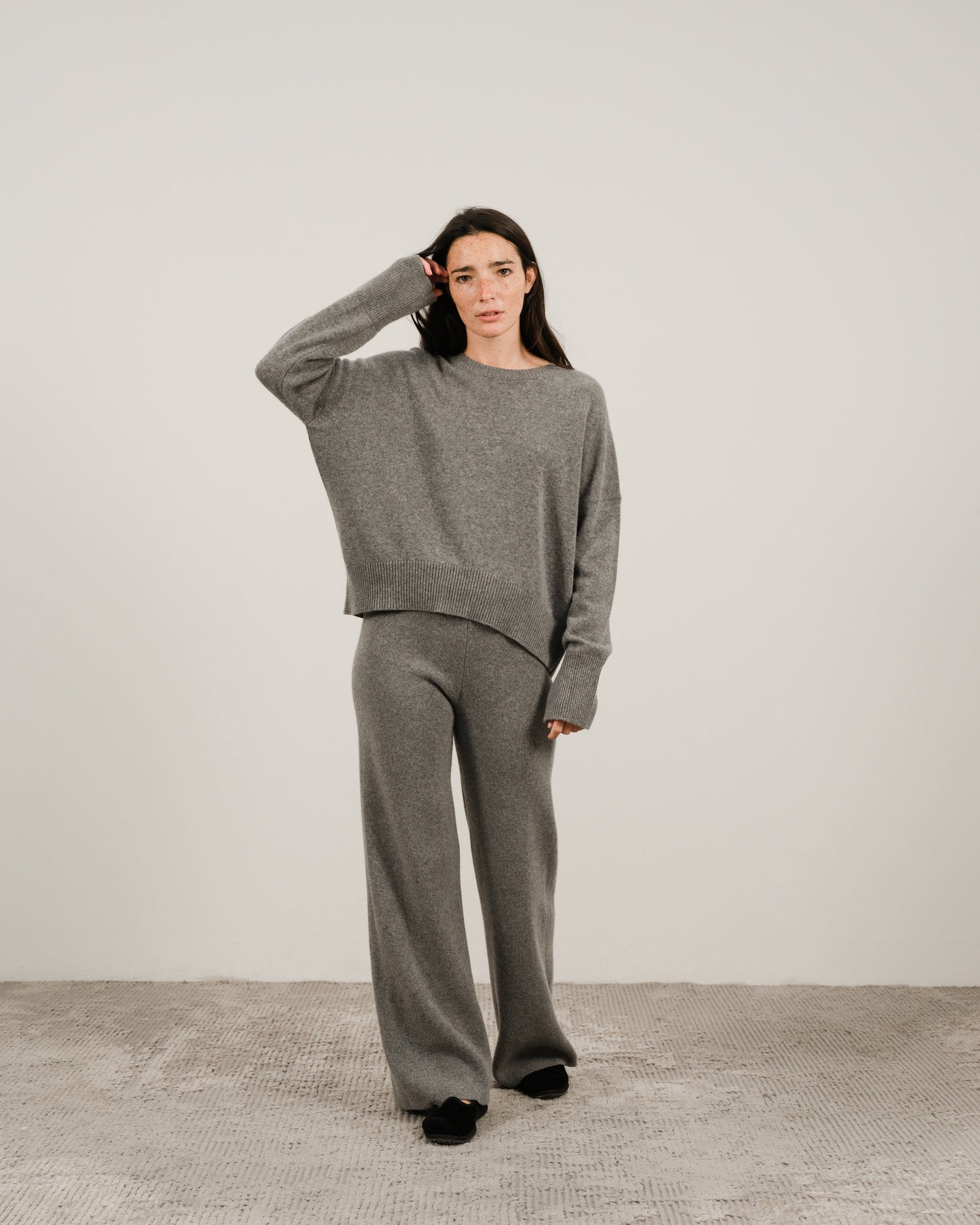 Model wearing a grey oversized cashmere mix crewneck sweater with matching wide-leg pants in a studio.
