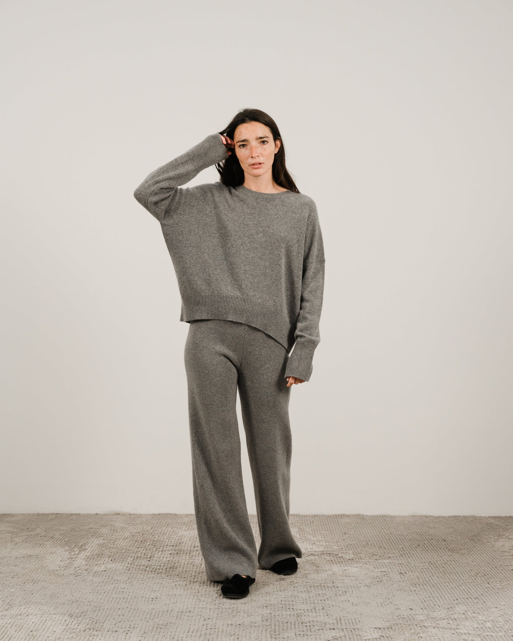 Model wearing a grey oversized cashmere mix crewneck sweater with matching wide-leg pants in a studio.