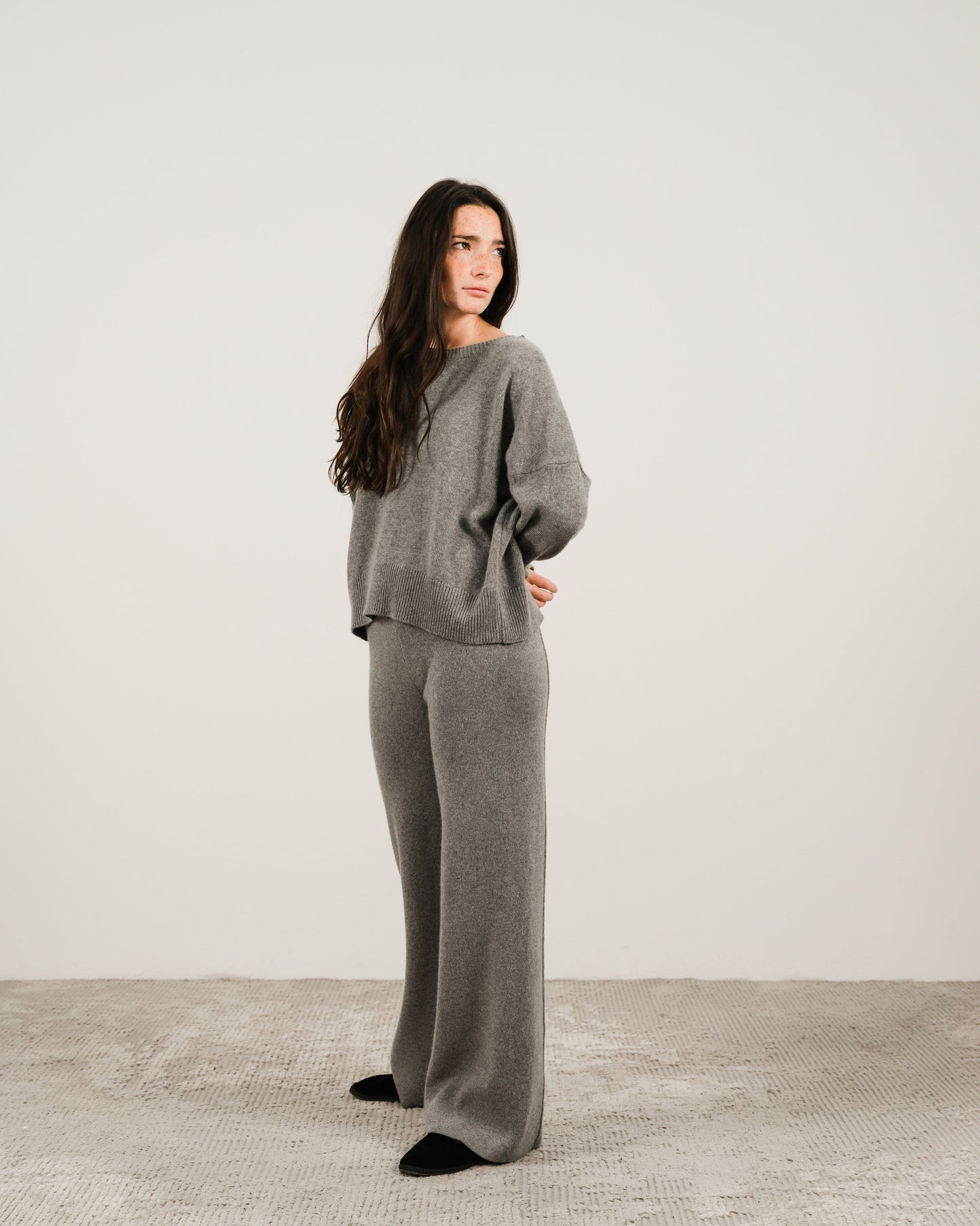 Woman in grey cashmere mix crewneck sweater with matching wide-leg pants standing in a studio setting.