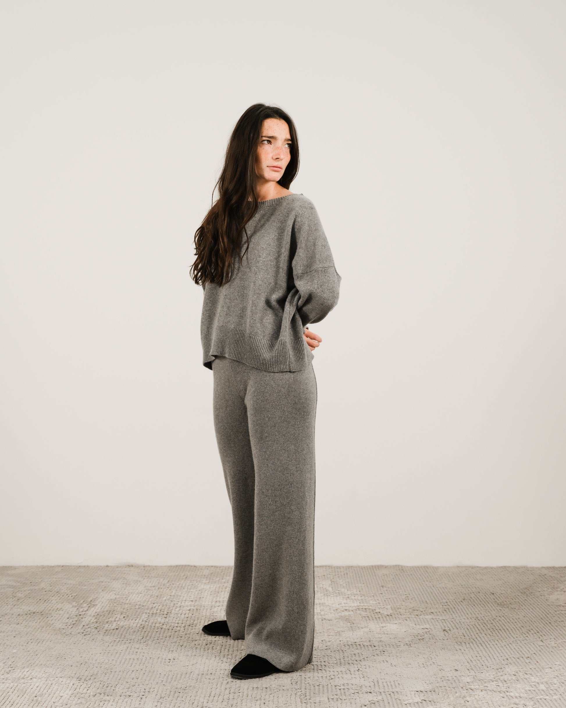Woman in grey cashmere mix crewneck sweater with matching wide-leg pants standing in a studio setting.