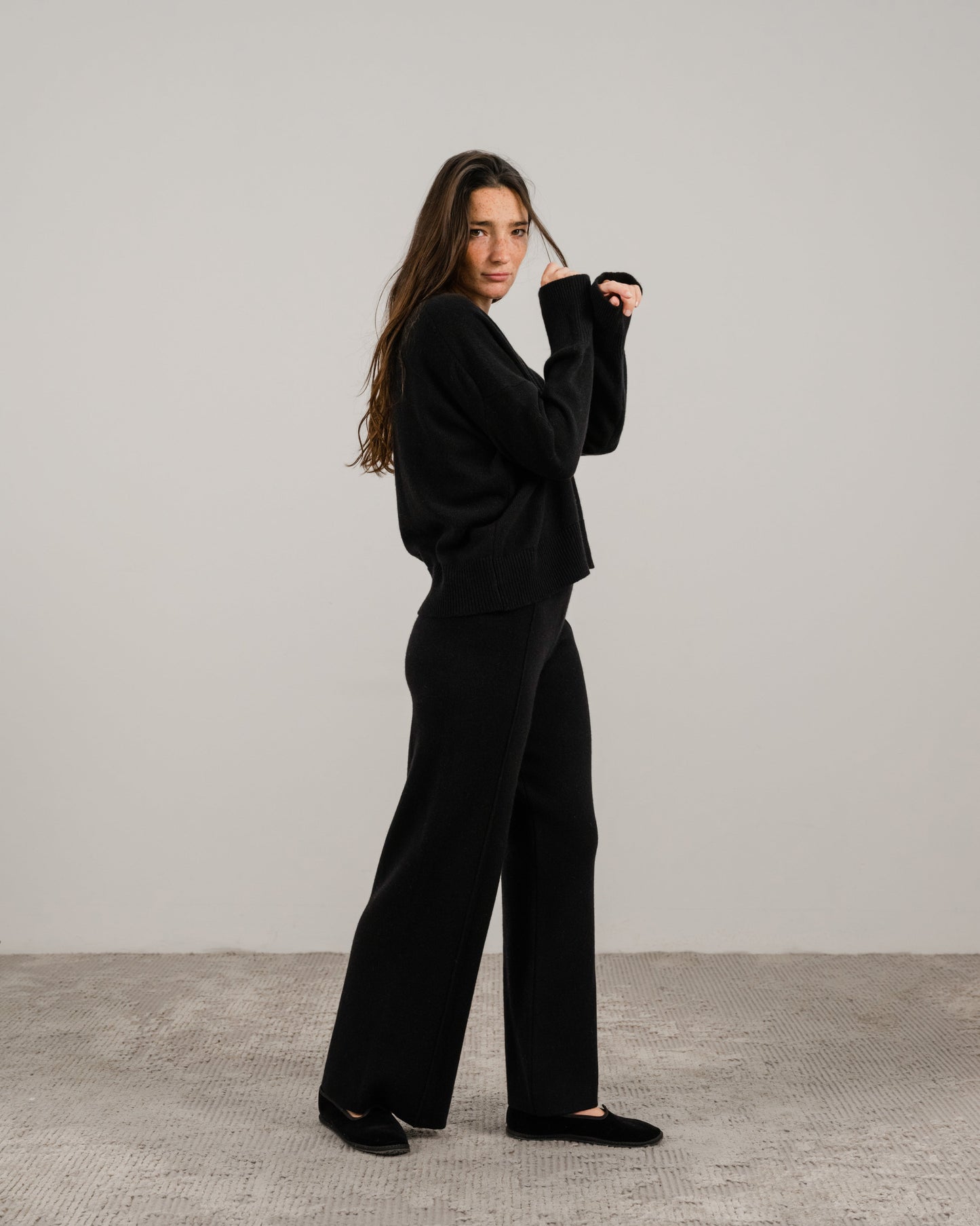 Full body side view of a woman in a black cashmere mix crewneck sweater with wide-leg pants