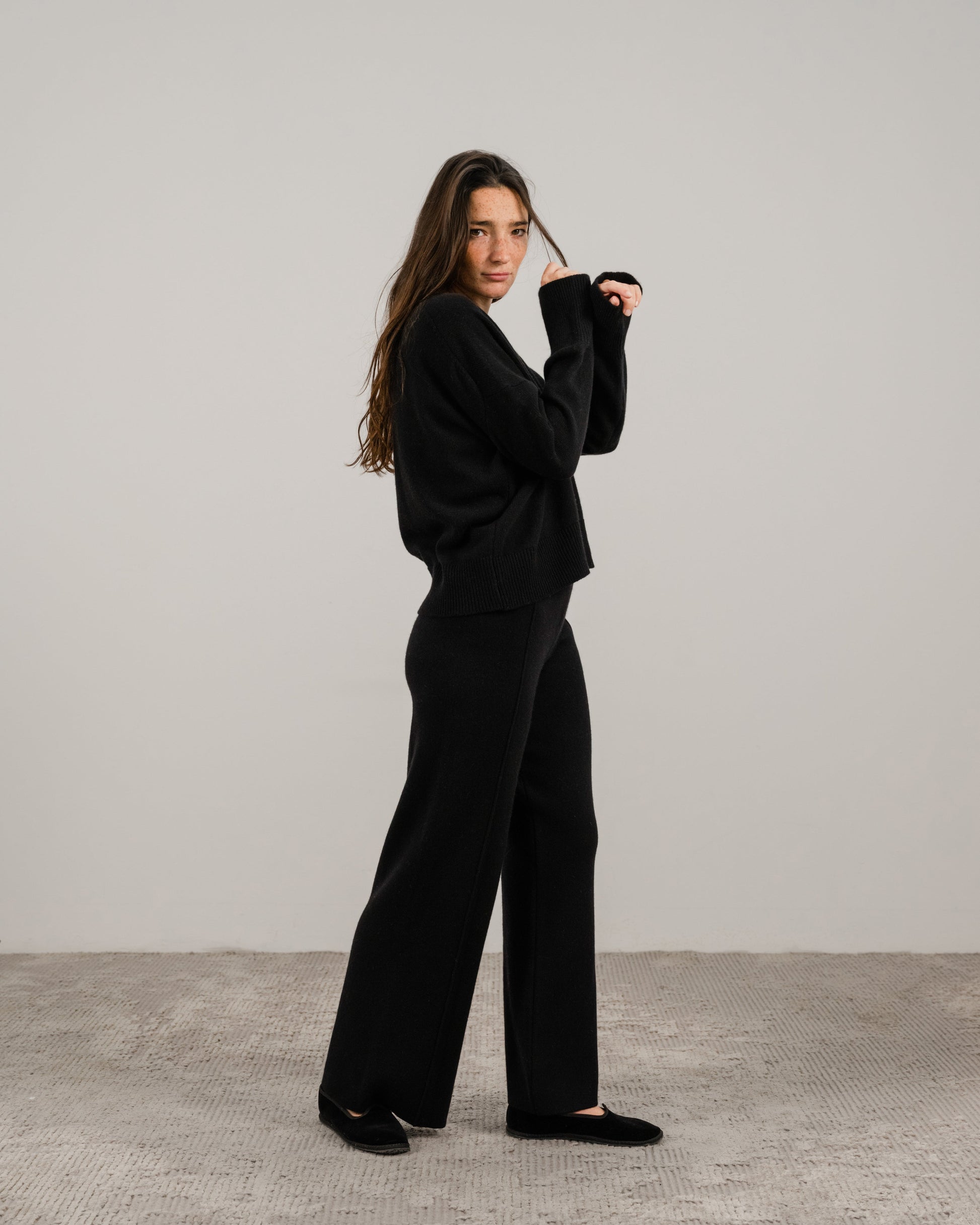 Full body side view of a woman in a black cashmere mix crewneck sweater with wide-leg pants