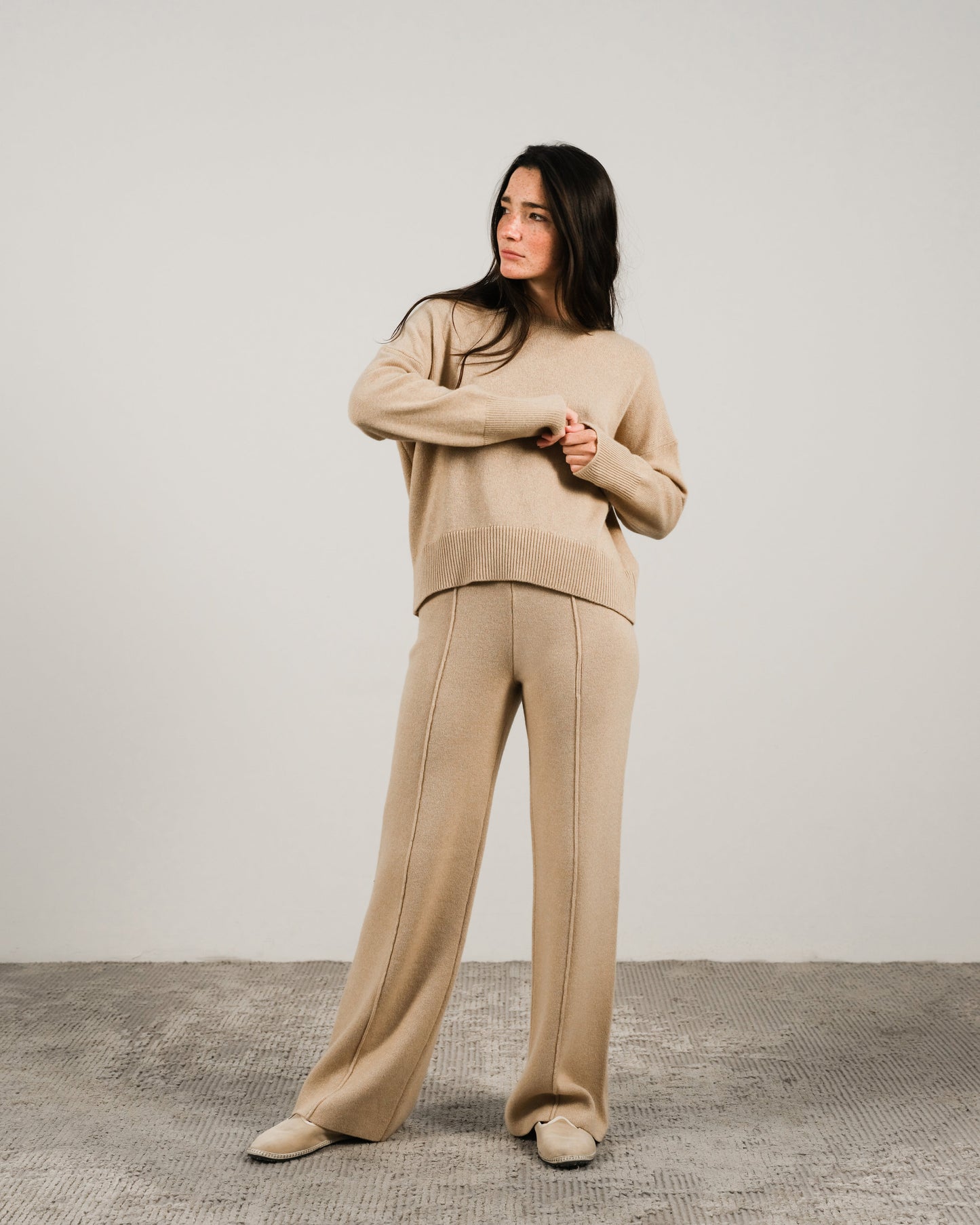 Full-length view of a model wearing a beige cashmere mix crewneck sweater and matching wide-leg pants in a studio