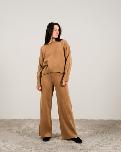Front view of a woman in camel cashmere mix crewneck sweater and matching wide-leg pants in a neutral studio.