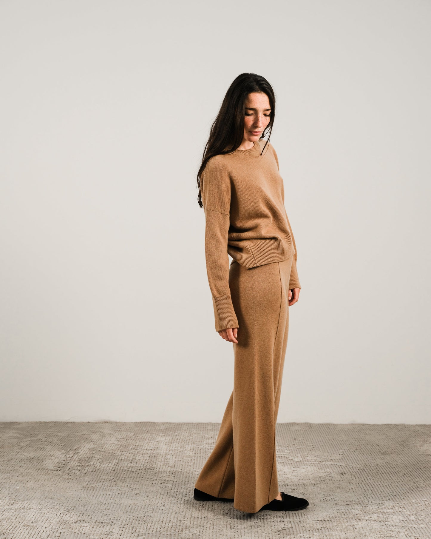 Side view of a woman wearing a camel cashmere mix crewneck sweater with matching wide-leg pants