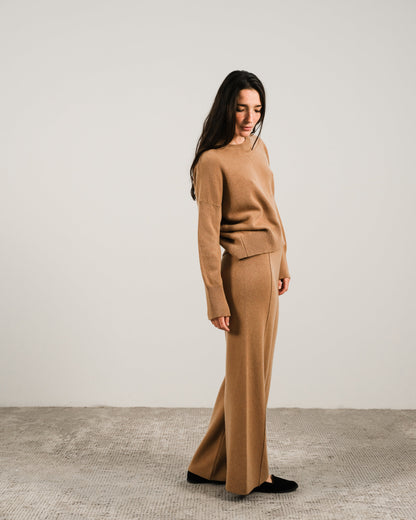 Side view of a woman wearing a camel cashmere mix crewneck sweater with matching wide-leg pants
