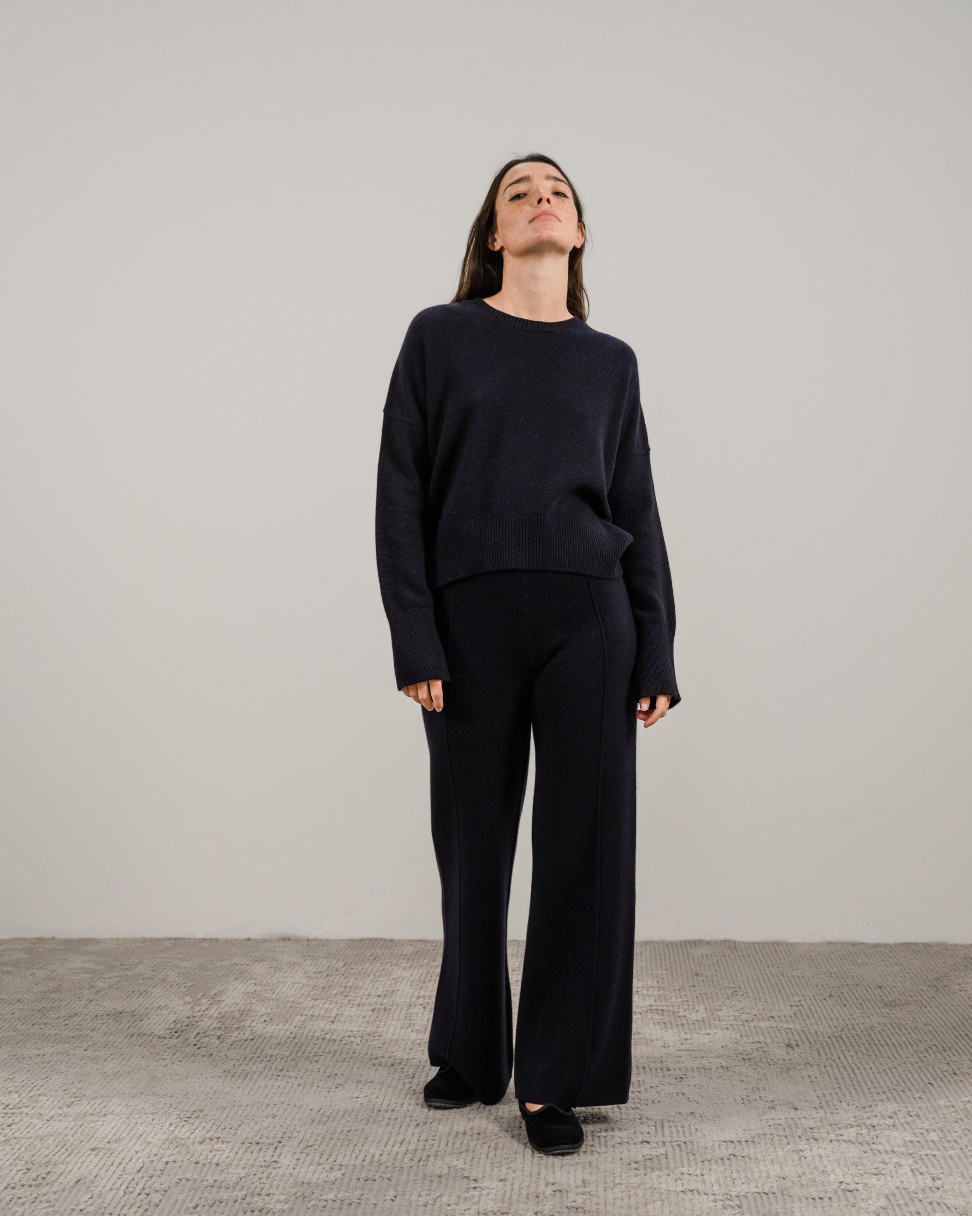 Model wearing navy cashmere mix crewneck sweater and matching dark pants against a neutral backdrop.