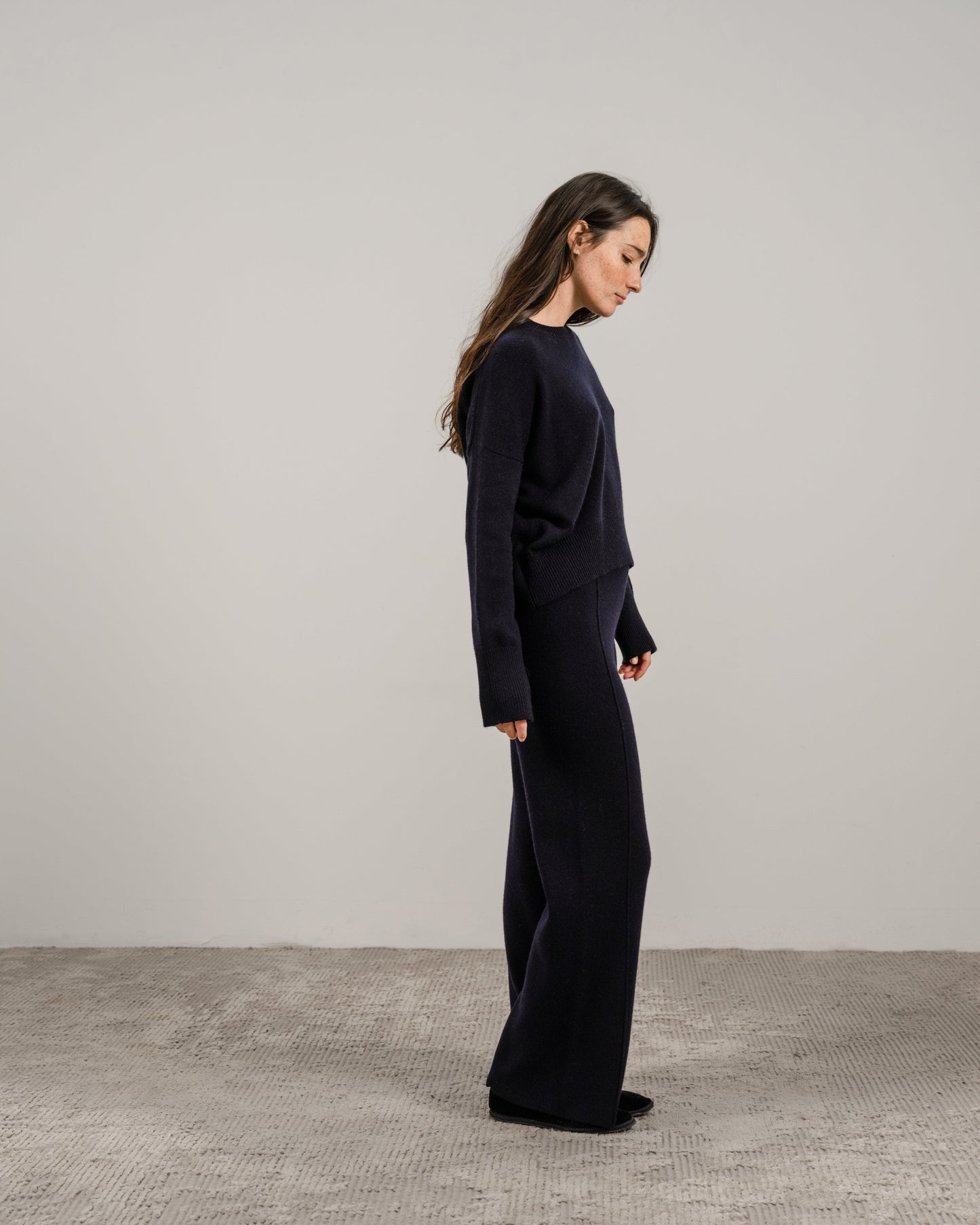 Side profile of a model in navy cashmere mix crewneck sweater and matching wide-leg pants