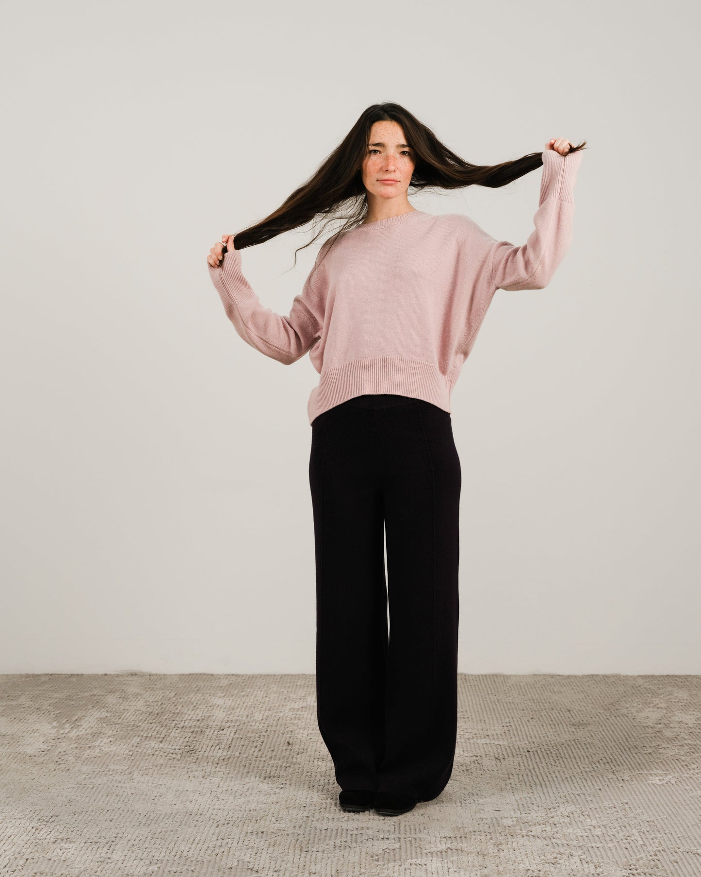 Model wearing a soft pink cashmere mix crewneck sweater with black wide-leg pants.