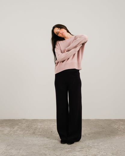 Model wearing a soft pink cashmere mix crewneck sweater with wide-leg black pants against a neutral backdrop.