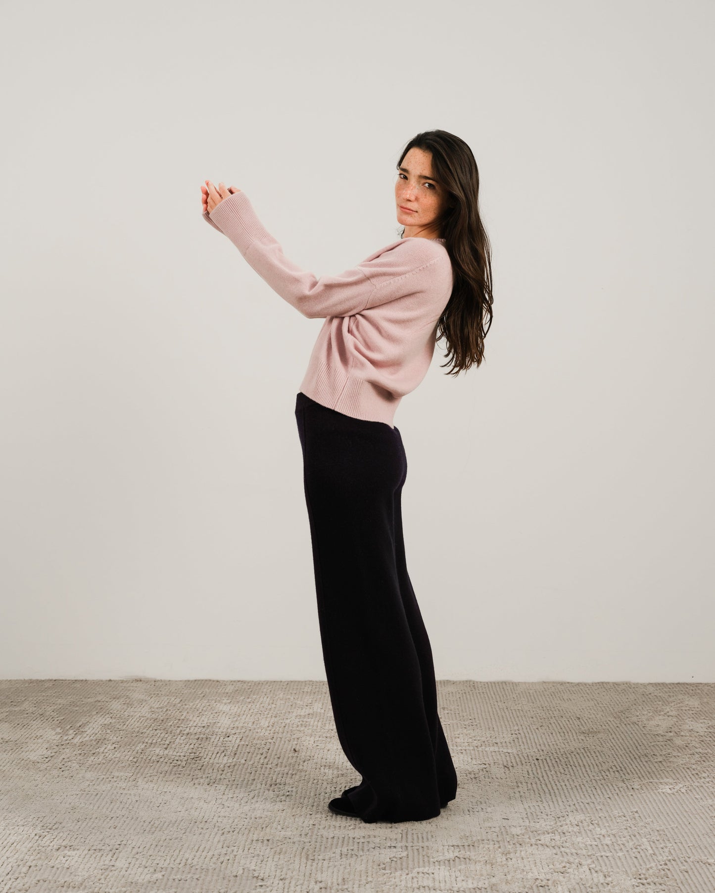 Model wearing pale pink cashmere mix crewneck sweater with black wide-leg pants in a side pose