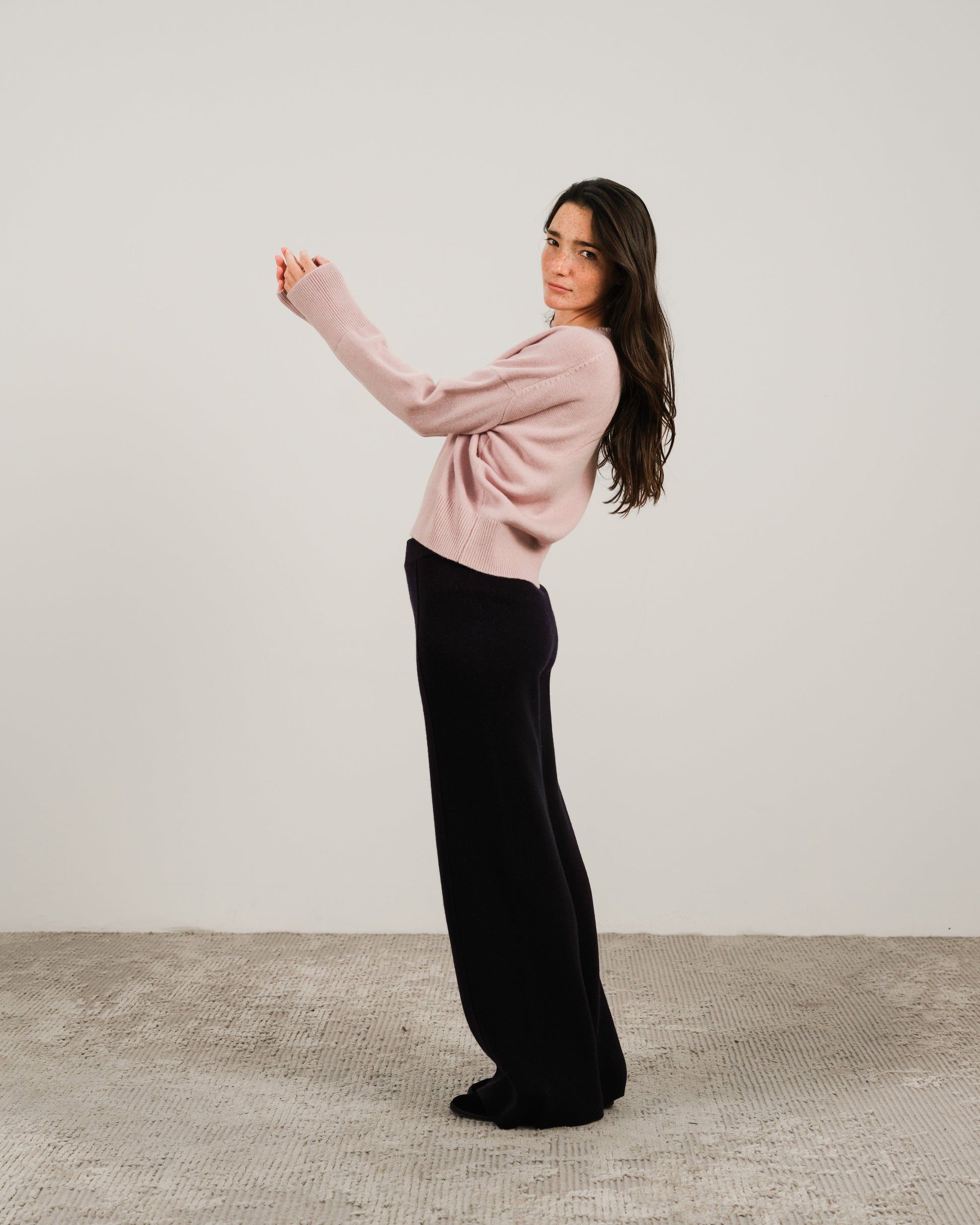 Model wearing pale pink cashmere mix crewneck sweater with black wide-leg pants in a side pose