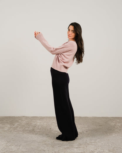 Model wearing pale pink cashmere mix crewneck sweater with black wide-leg pants in a side pose