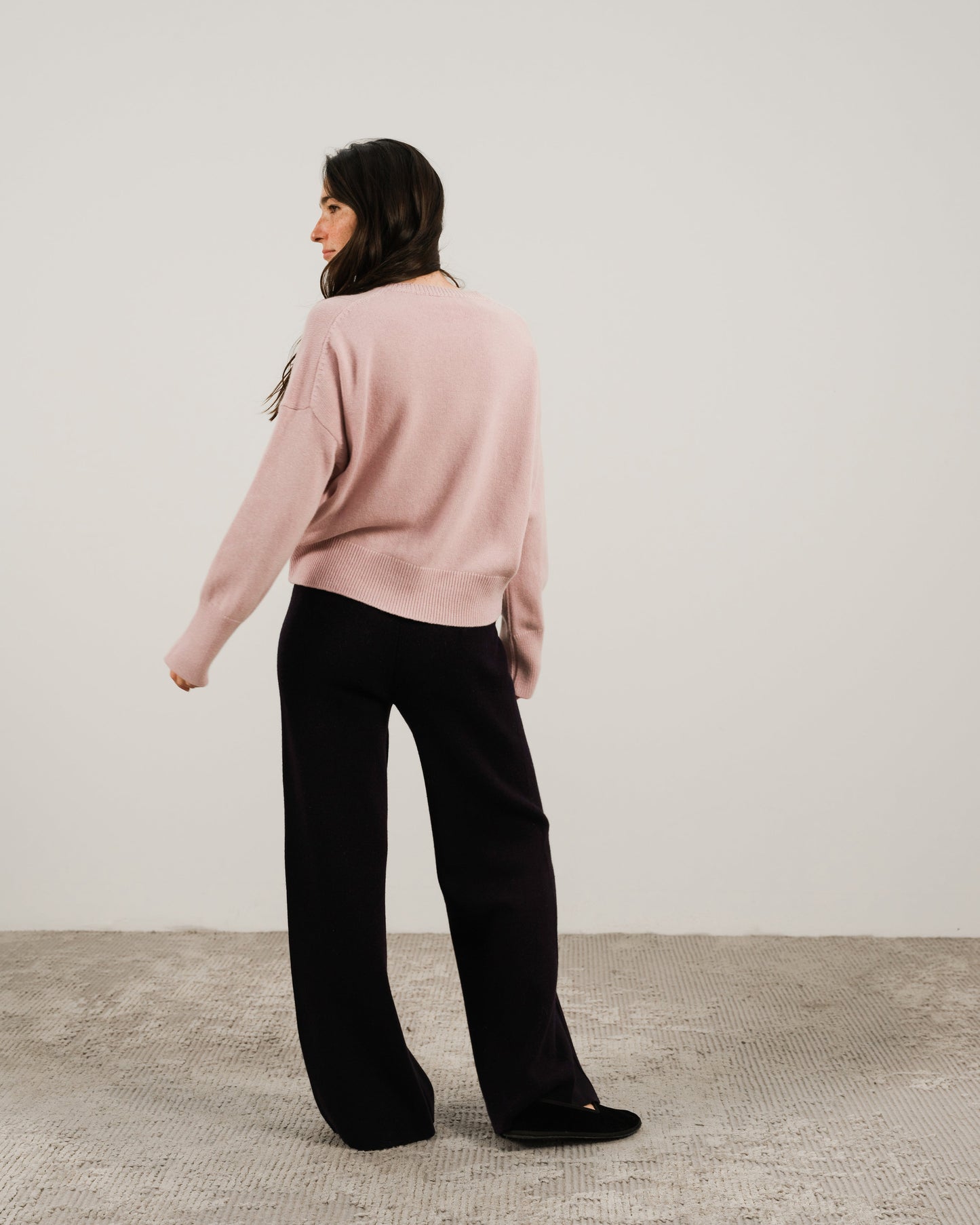 Back view of model in pastel pink cashmere mix crewneck sweater with relaxed fit and ribbed hem