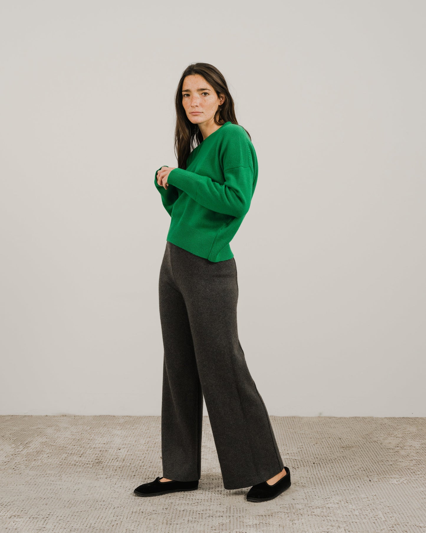 Full body shot of a model in a bright green cashmere mix crewneck sweater with dark gray wide-leg pants