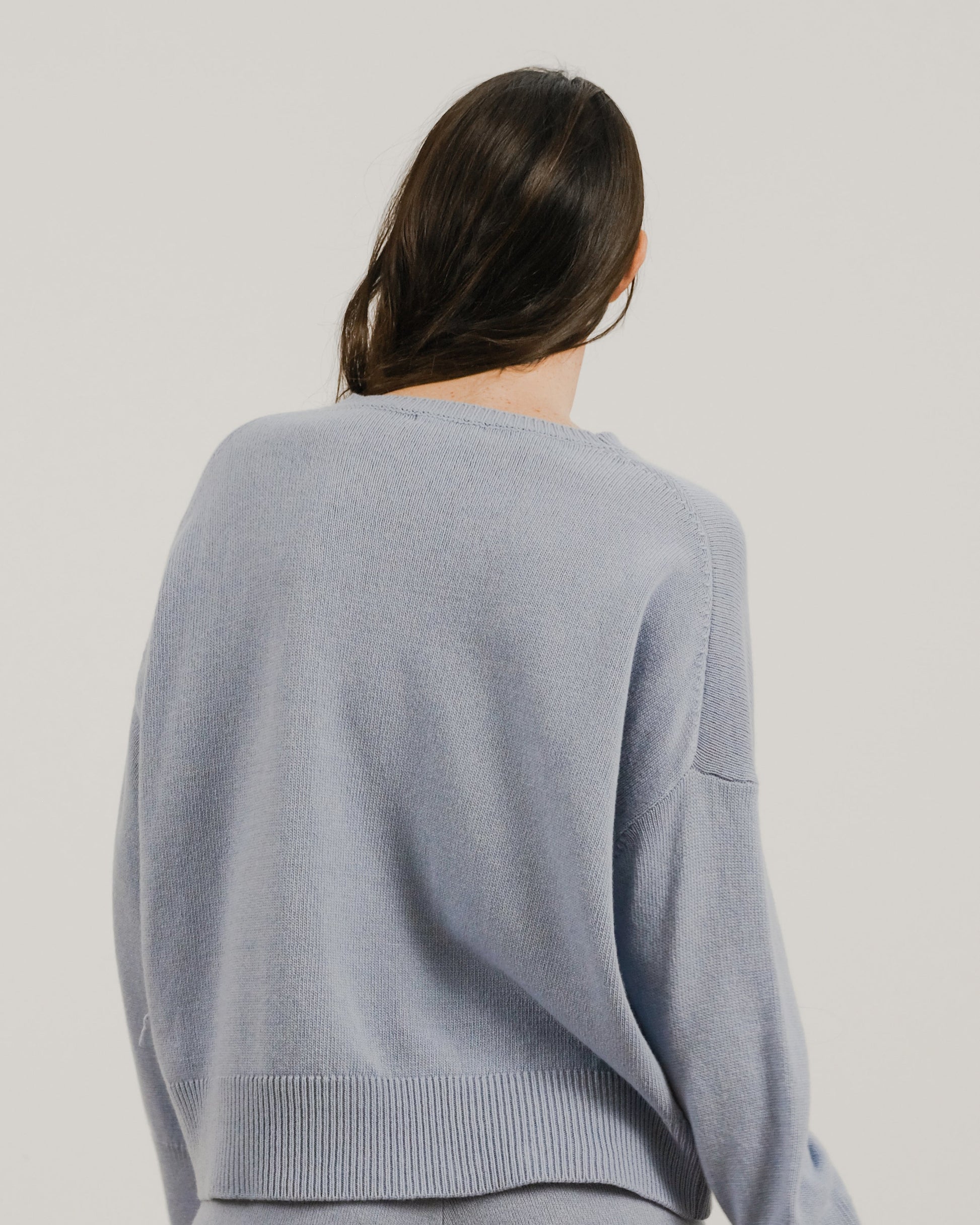 Back view of a loose light blue cashmere mix crewneck sweater on a model with a ribbed hem