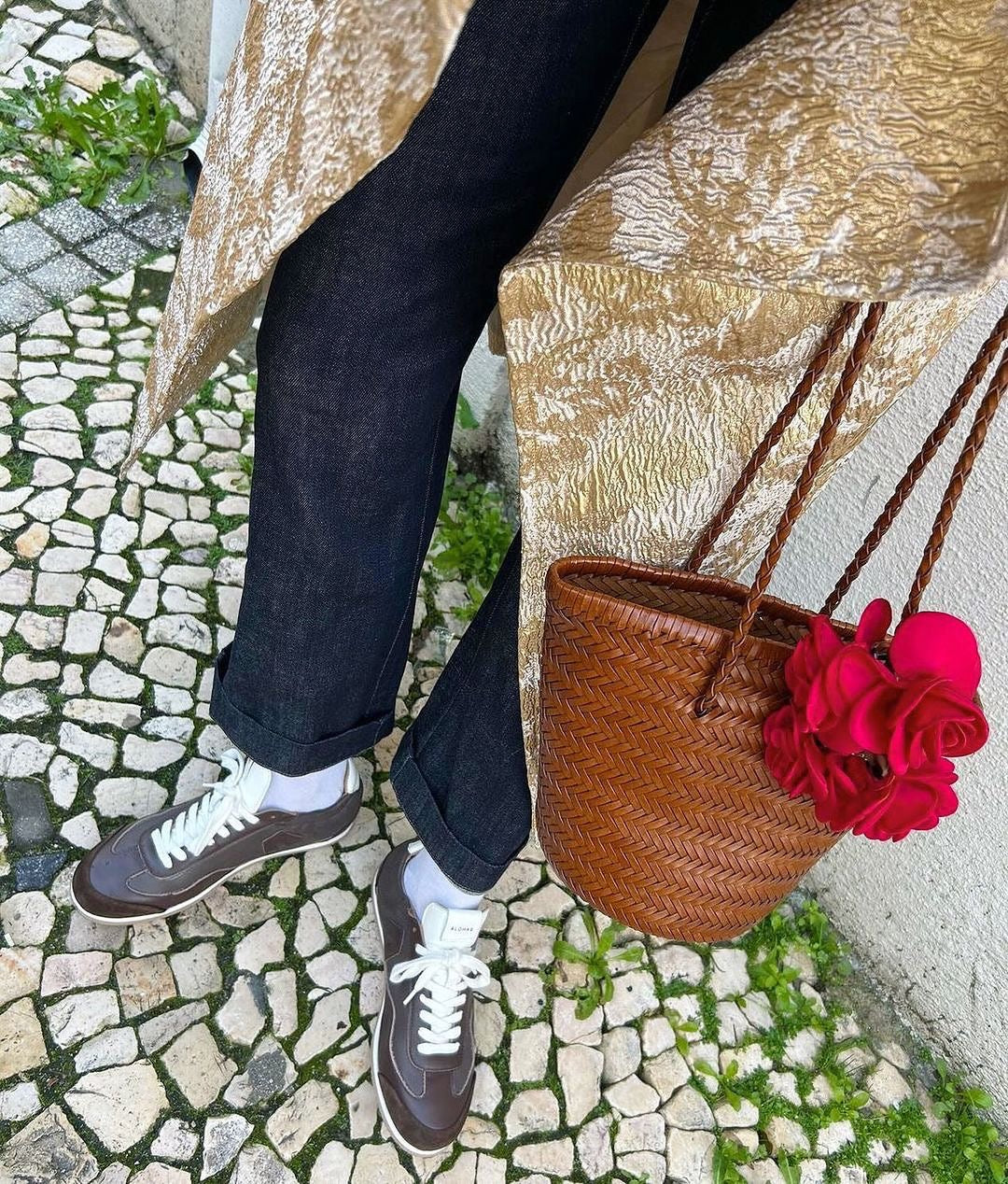 Brown handwoven leather shoulder bucket bag with braided straps and a bright pink flower accessory
