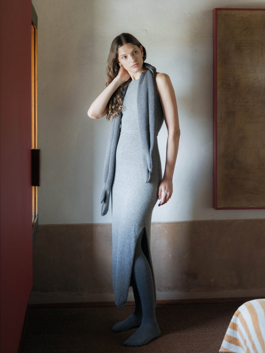 Model wearing a light gray sleeveless knit maxi dress with a long scarf draped around the neck.