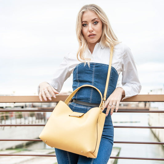 Clio yellow pebbled leather bucket bag worn crossbody by a model on a rooftop