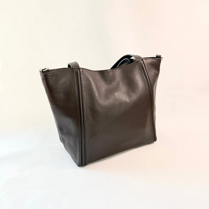 A dark brown pebbled leather tote bag with top handles, photographed on a plain off-white background.