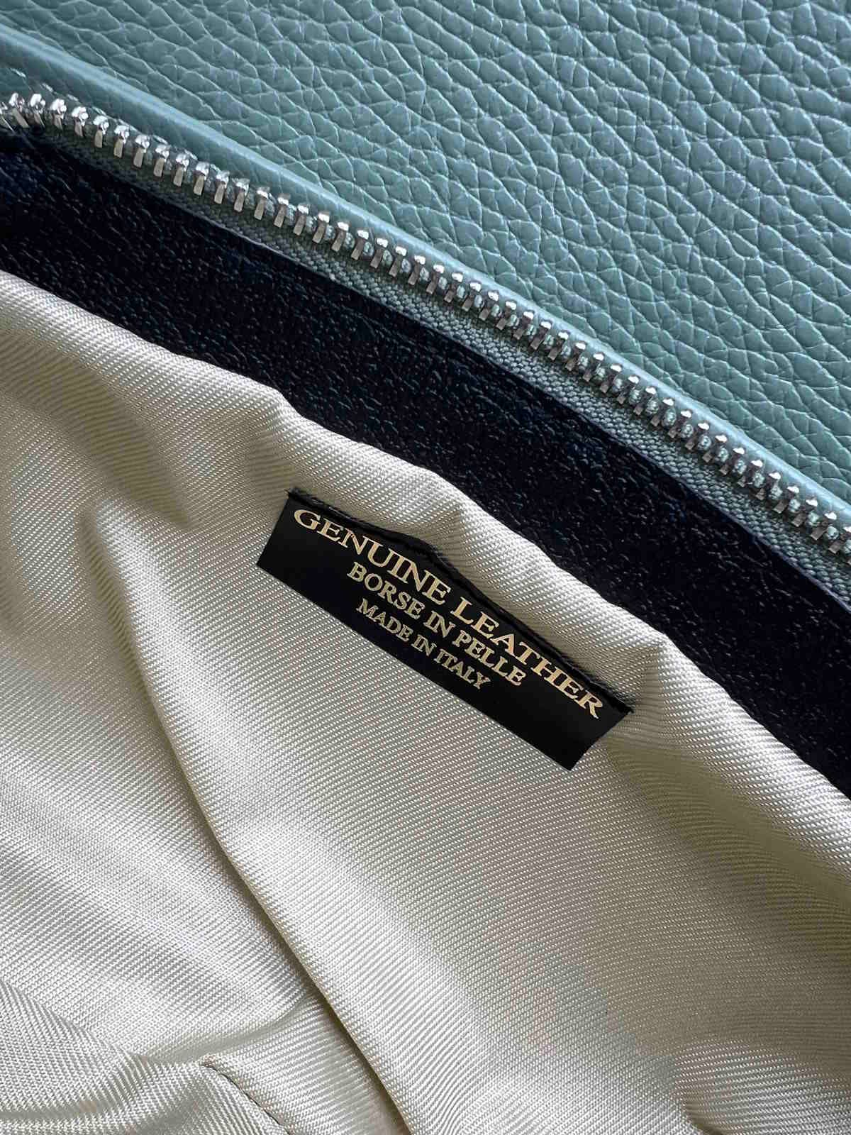 Close-up of the interior of a leather bag with a 'Genuine Leather, Made in Italy' label, featuring a zipper and textured leather surface.