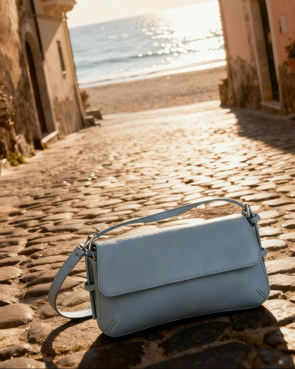 Light blue handbag on a cobblestone street with ocean view