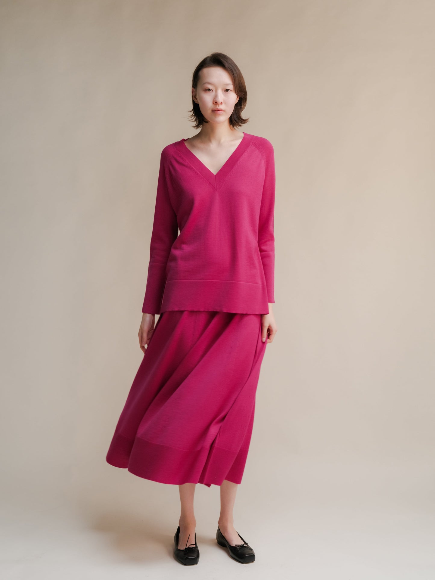 Magenta V-neck knit top paired with a matching 3D-knit merino wool A-line skirt on a model