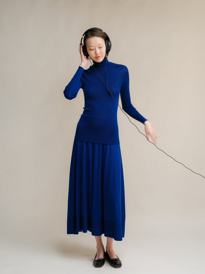 Model wearing cobalt blue extra fine merino wool A-line 3D-knit skirt with a matching knit top and headphones.