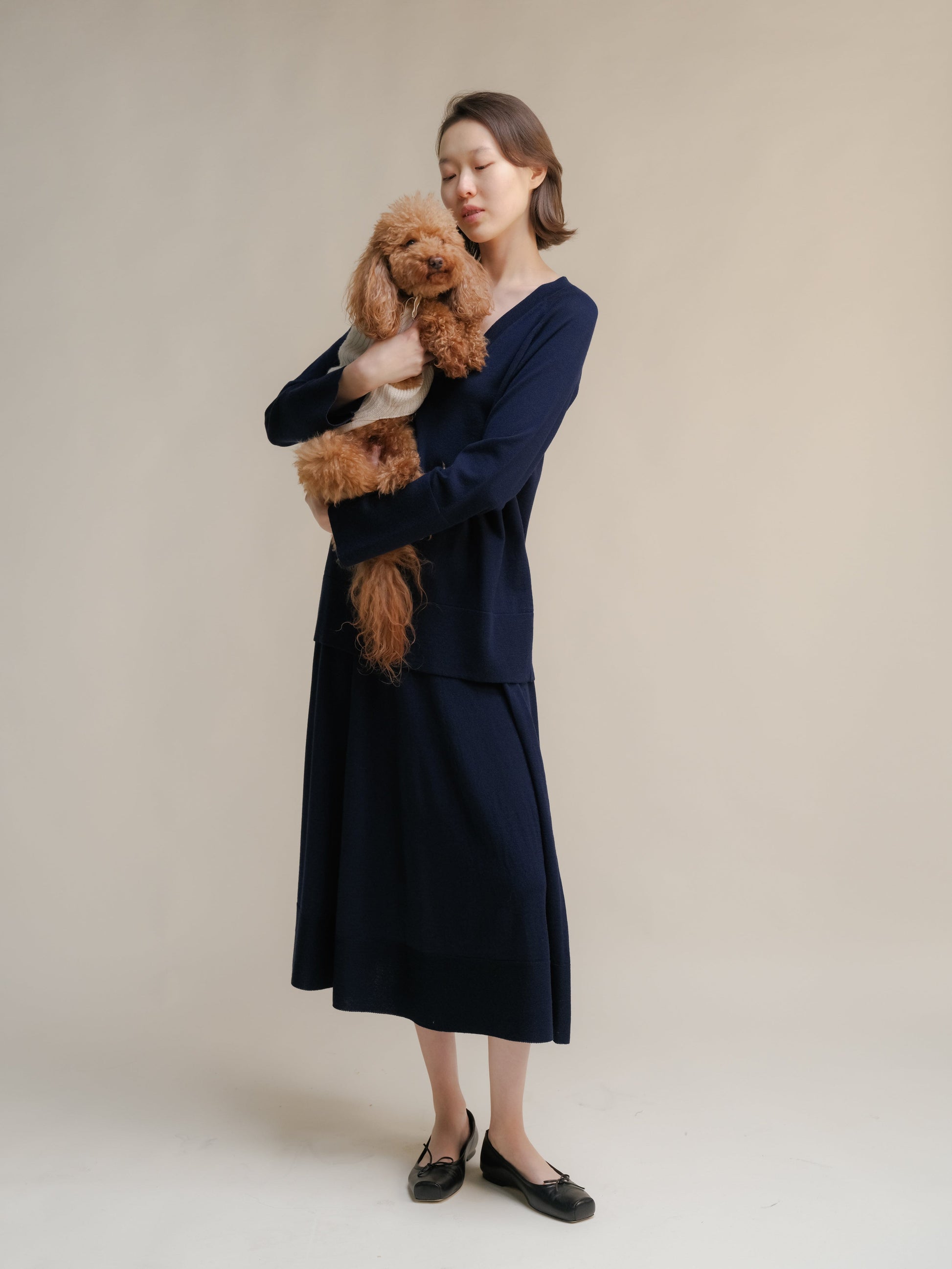 Woman in navy 3D-knit merino wool A-line skirt with a matching top, holding a fluffy brown dog.