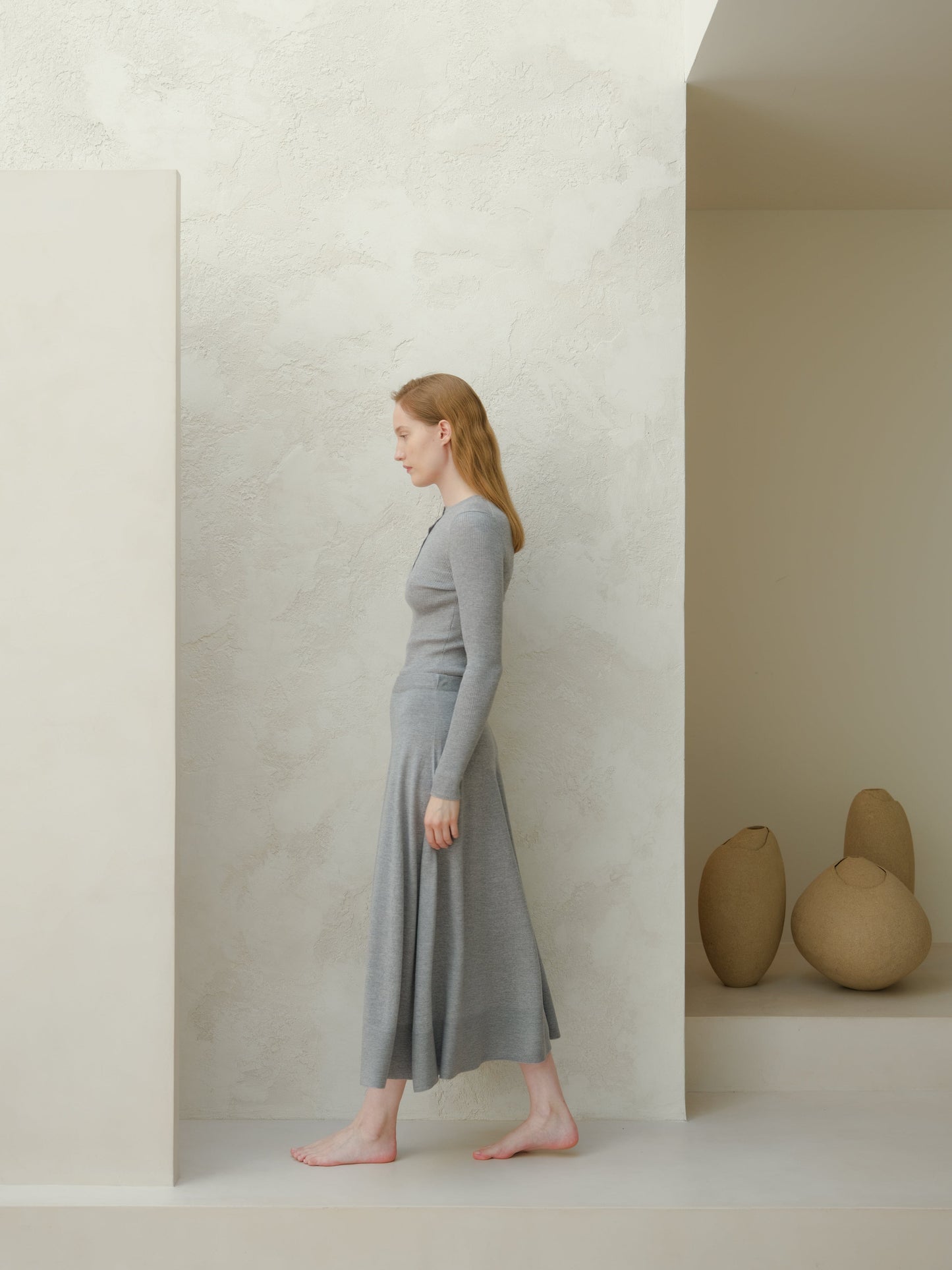 Side profile of a woman wearing a gray 3D knit merino wool A-line midi skirt with a matching top