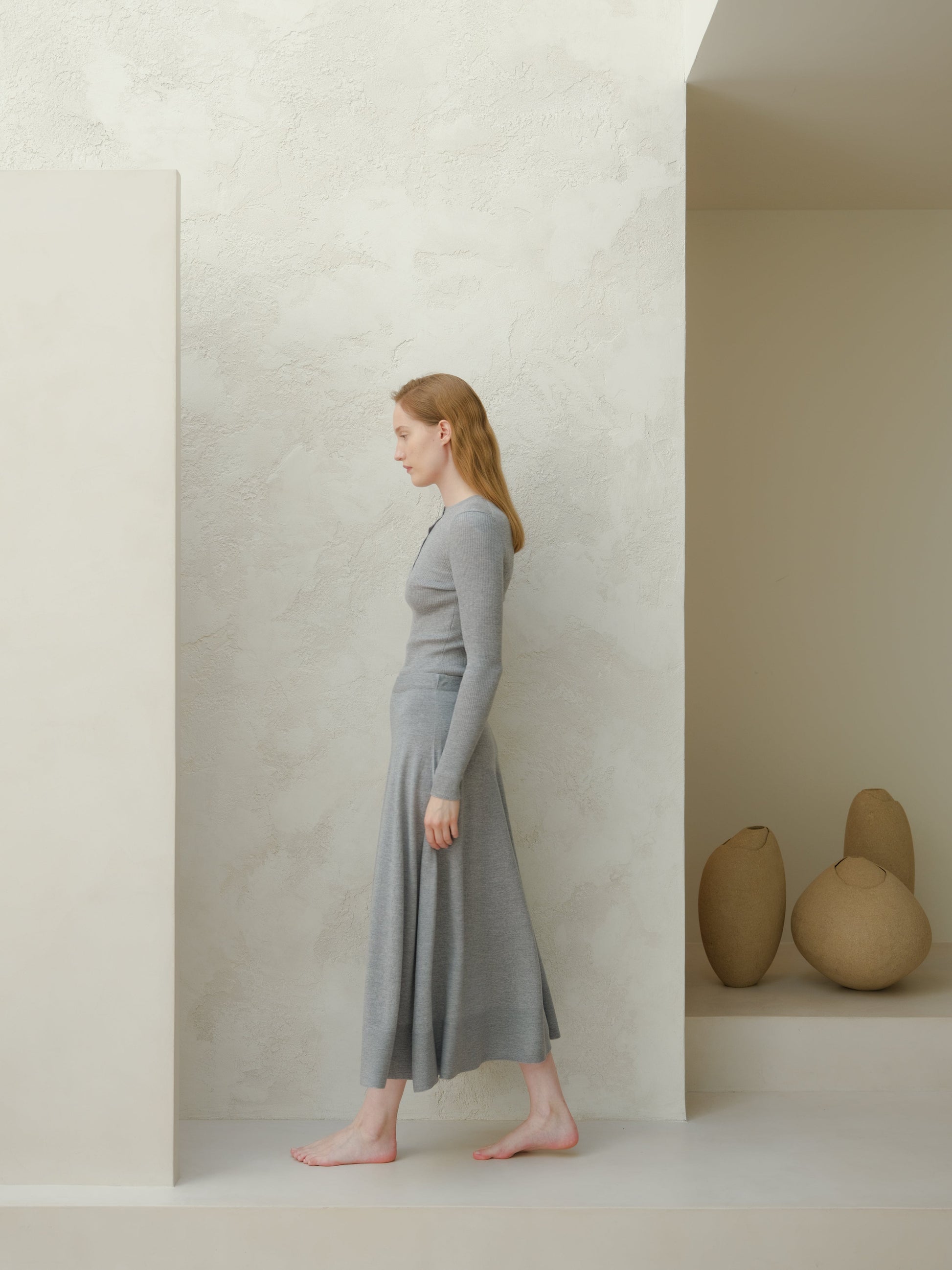 Side profile of a woman wearing a gray 3D knit merino wool A-line midi skirt with a matching top