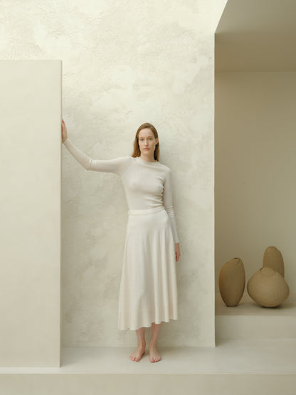 Ivory 3D-knit merino wool A-line midi skirt with a matching knit top, model standing barefoot against a pale textured wall.