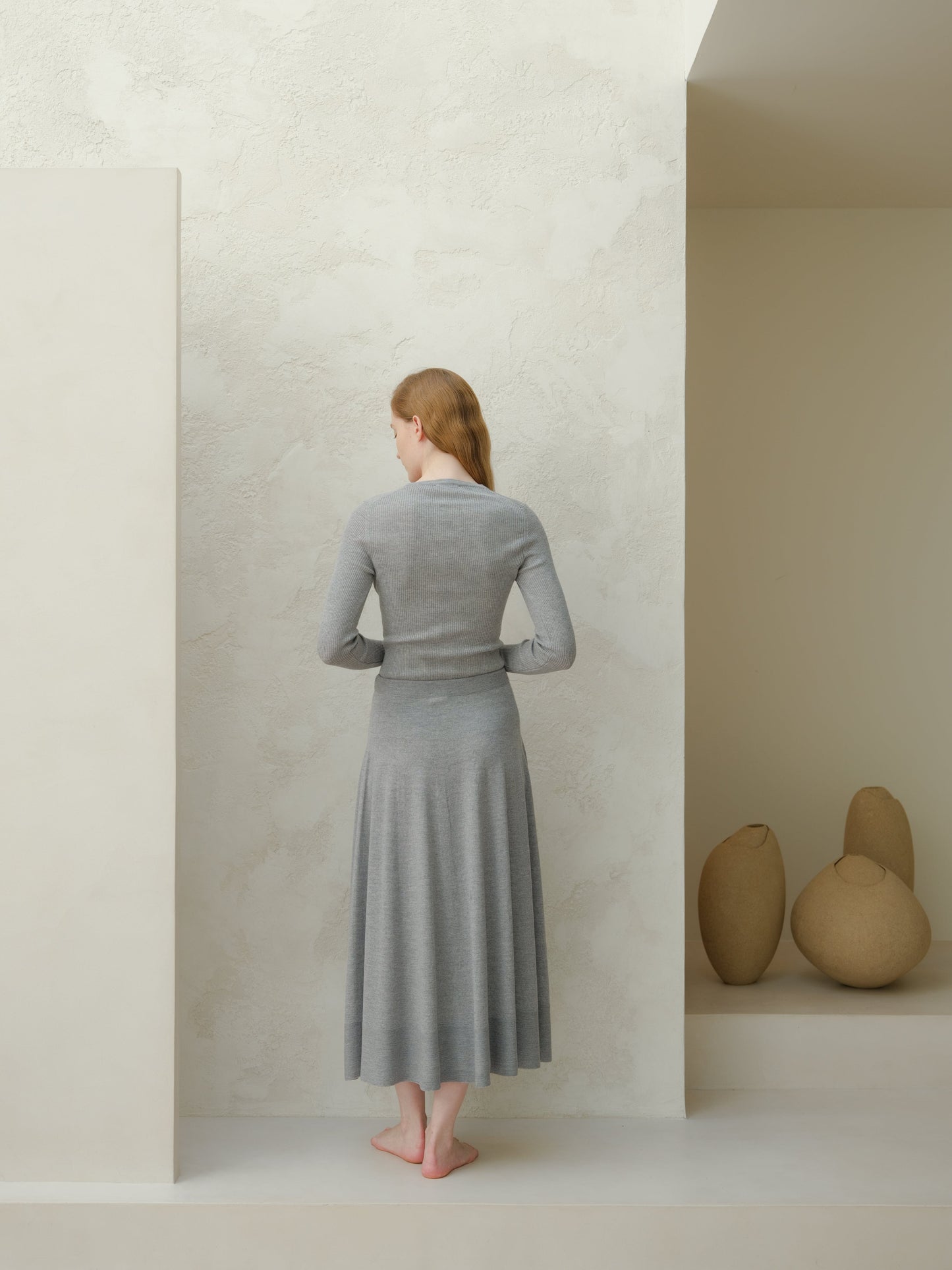 Back view of a woman wearing a gray 3D knit merino wool A-line midi skirt