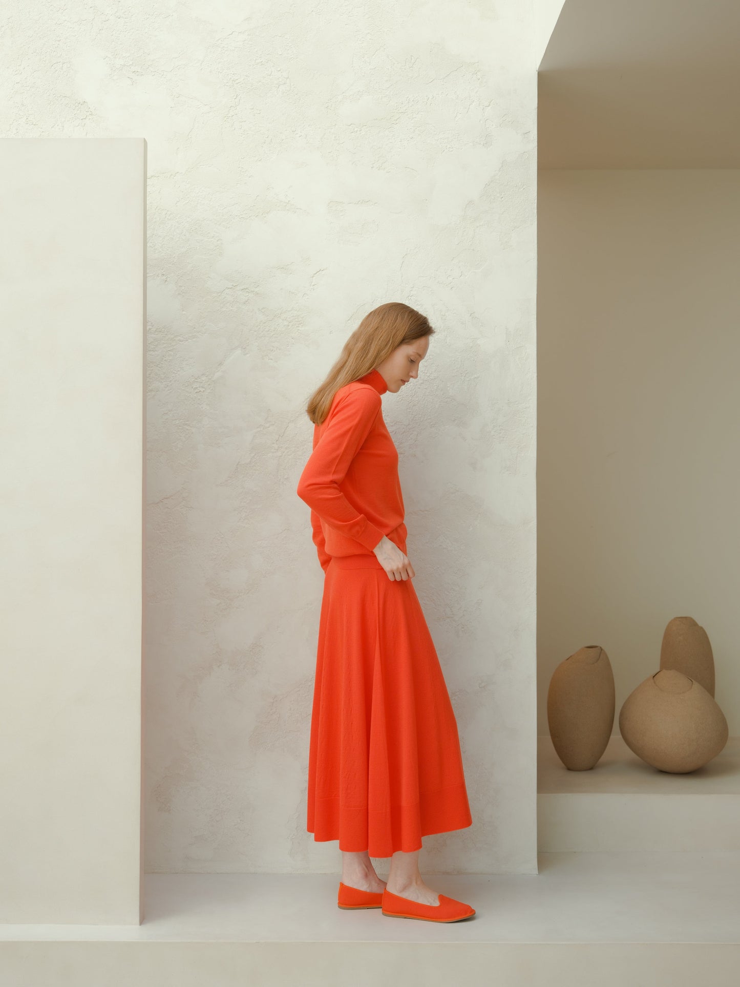 Side view of a model in a bright orange extra fine merino wool A-line skirt with a matching sweater.