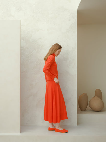 Side view of a model in a bright orange extra fine merino wool A-line skirt with a matching sweater.