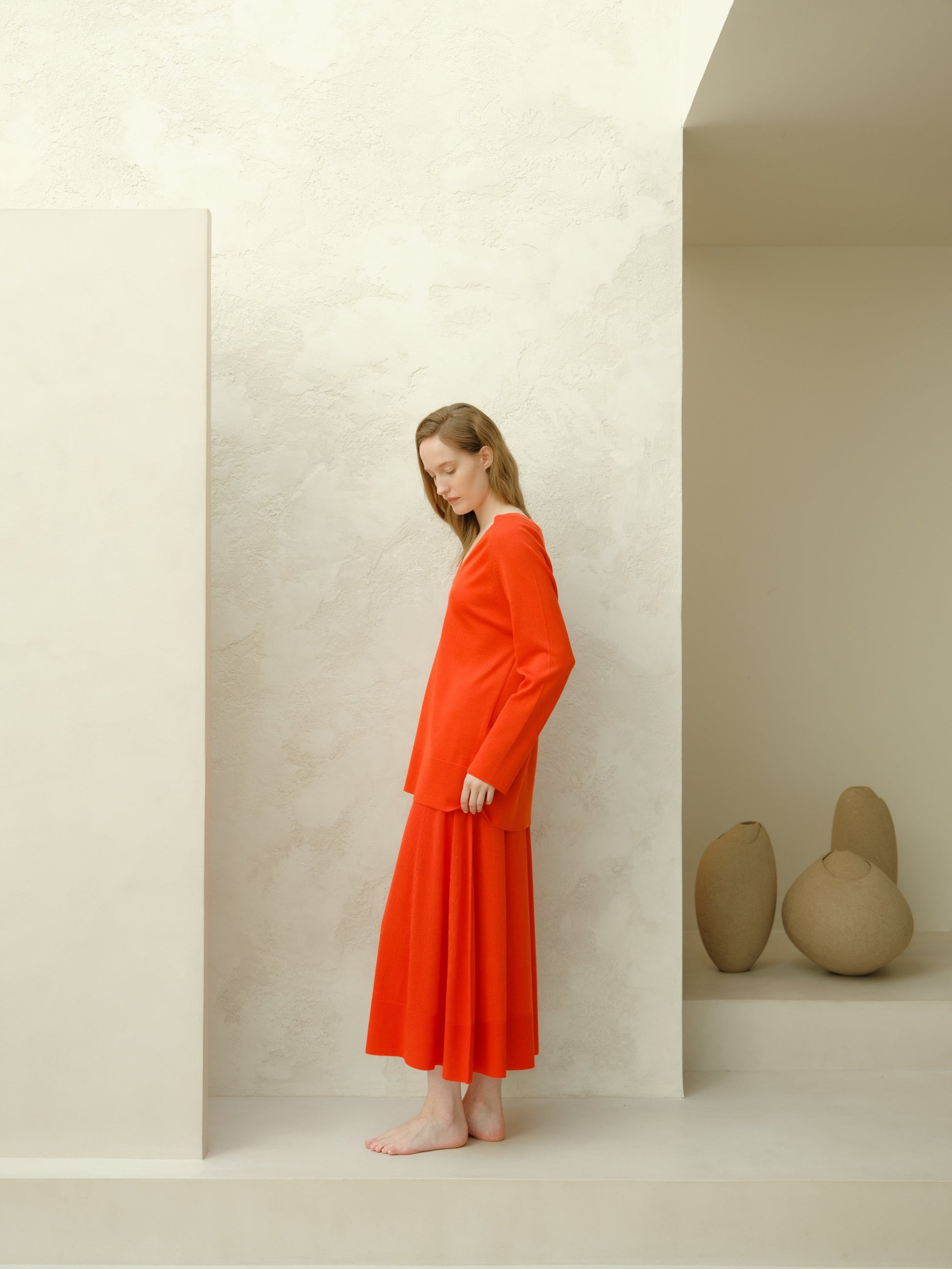 Model wearing bright orange merino wool A-line skirt with a matching knit top in a pale studio setting.