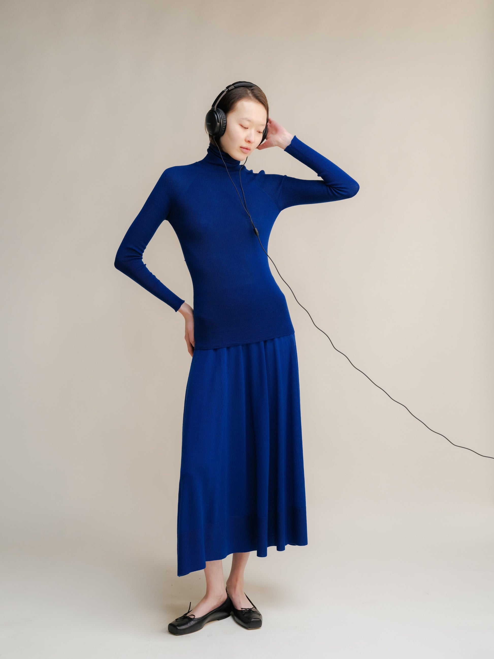 Model wearing cobalt blue merino wool A-line 3D-knit skirt with a matching top and headphones.