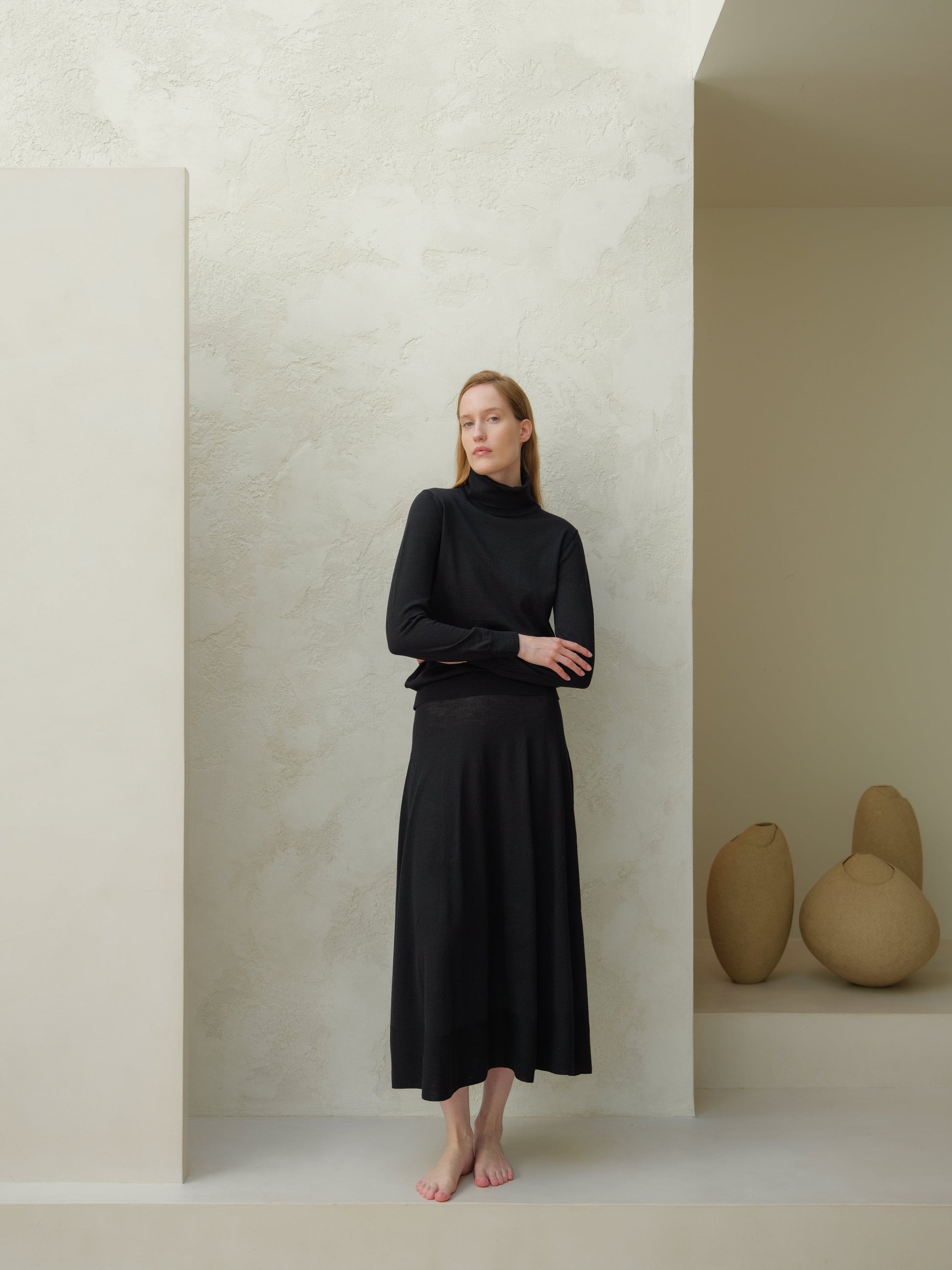 Full-length view of a model wearing a black 3D-knit merino wool A-line skirt paired with a black turtleneck