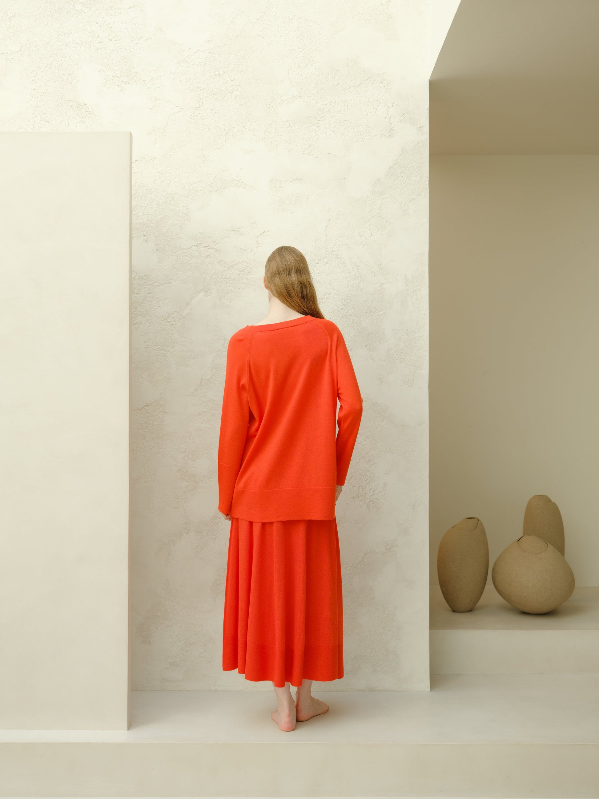 Back view of a model wearing a bright red merino wool A-line skirt against a textured cream wall.