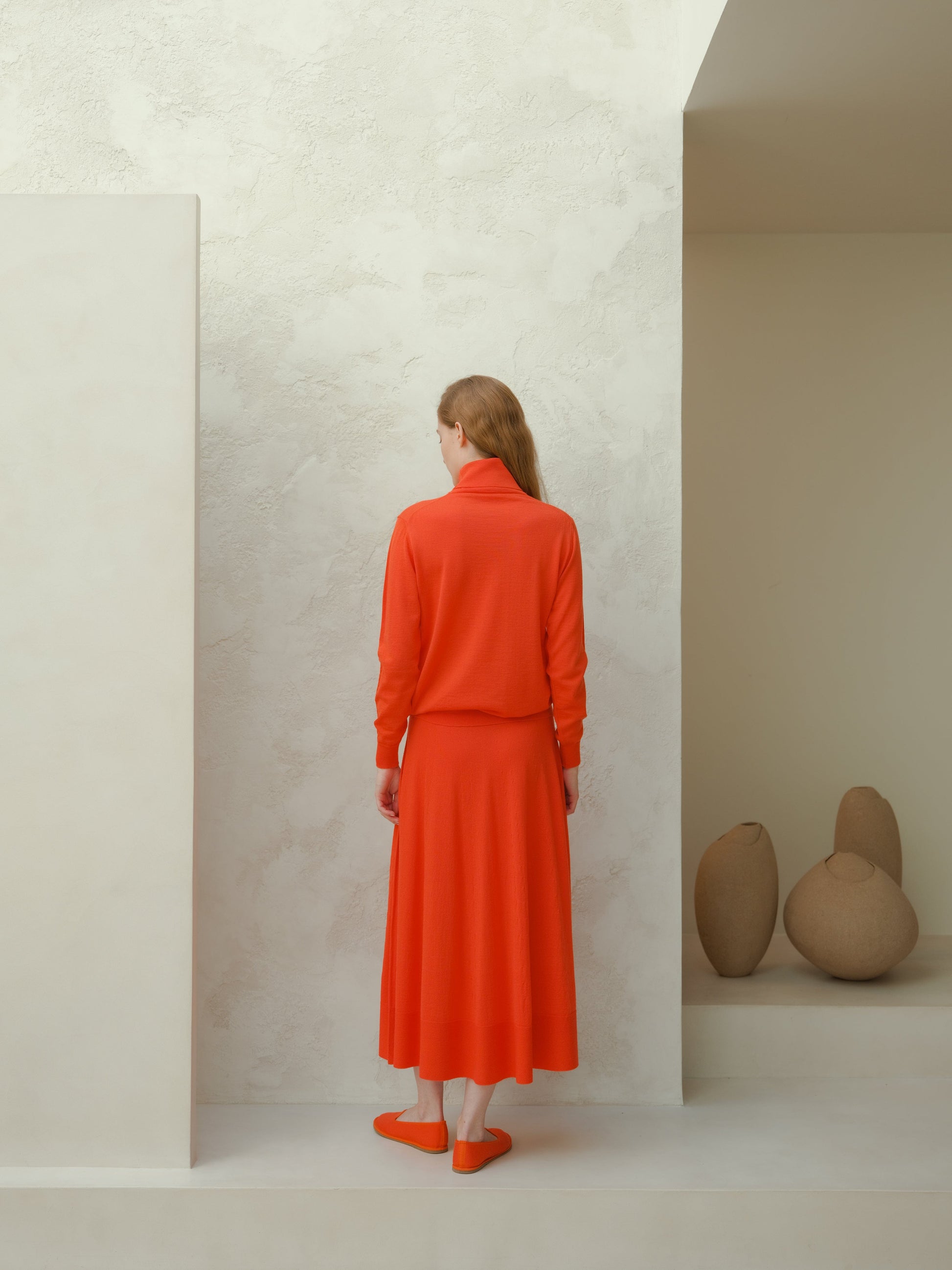 Back view of a model wearing a bright orange extra fine merino wool A-line skirt and matching sweater.