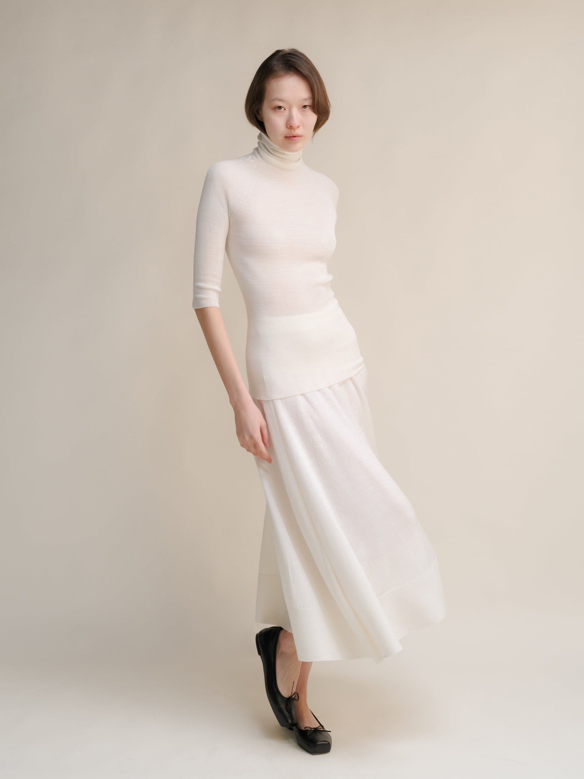 Model in ivory 3D Knit merino wool A-Line skirt with matching turtleneck in a full-length pose