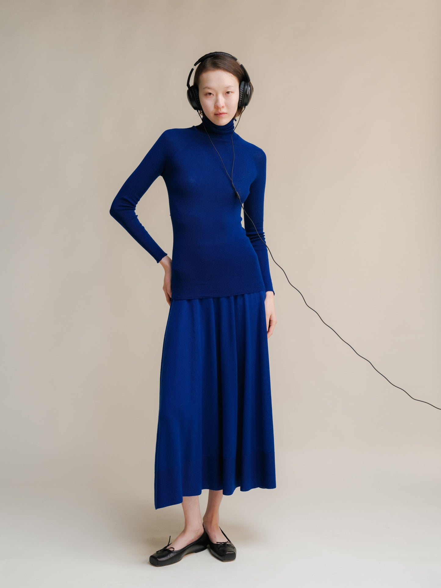 Model wearing cobalt blue 3D knit merino wool A-Line skirt with a matching turtleneck in a studio.