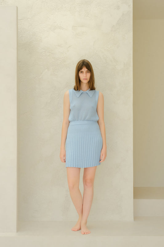 Woman wearing a light blue sleeveless top and skirt against a neutral background