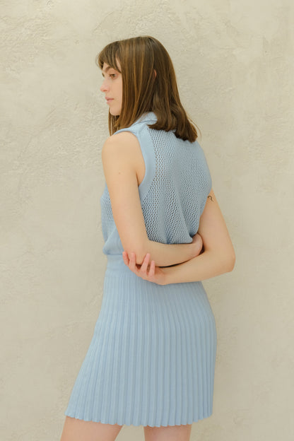 Woman wearing a light blue sleeveless top and skirt against a neutral background