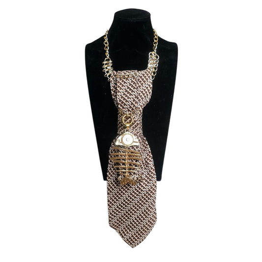 Beige patterned necktie displayed on a black bust with a gold chain and fish skeleton pendant.